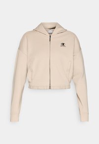 Κοντό μπεζ φούτερ με κουκούλα από απαλό ύφασμα, με φερμουάρ μπροστά, ρυθμιζόμενη κουκούλα και μικρό μαύρο λογότυπο στο στήθος.