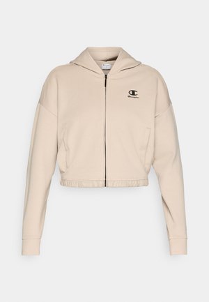 Prekratka bež majica s kapuljačom od mekanog tkanja, sa prednjim patentnim zatvaračem, podesivom kapuljačom i malim crnim logotipom na prsima.