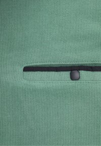 Vihreä ribbikangas, jossa on teksturoitu pinta; siinä on vaakasuora raitapussi mustalla reunuksella ja pyöreä musta nappisulku.