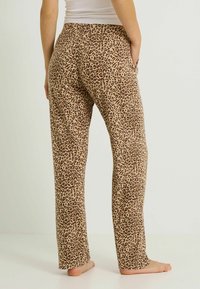 Pantalon de détente imprimé léopard en tissu doux et extensible. Il présente une coupe décontractée, des jambes droites et des poches latérales, avec un fond beige.