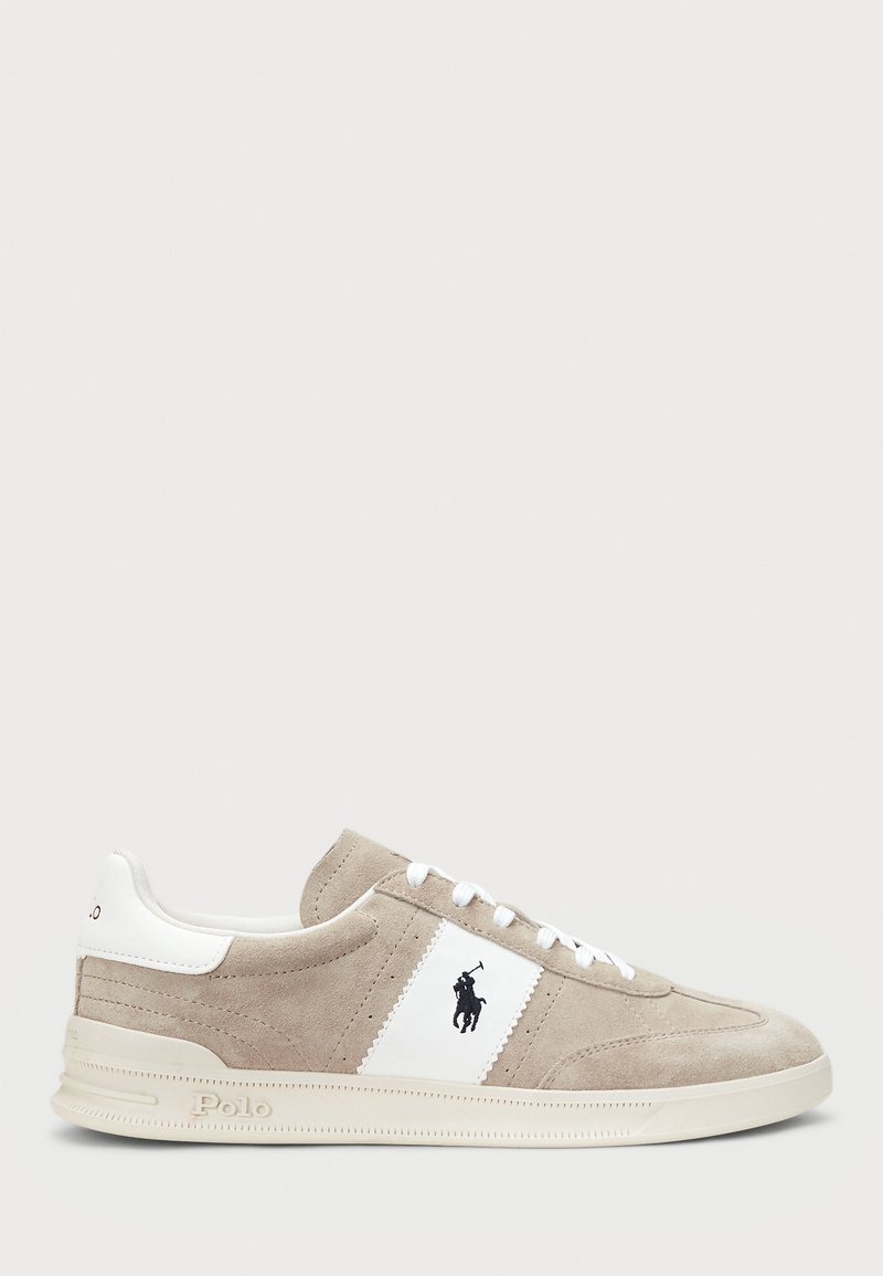 Sneaker in suede beige con accenti bianchi, caratterizzato da un patch con logo e lacci bianchi. Il design include una tomaia testurizzata e una suola piatta in gomma.