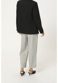 Blazer nero con un design strutturato e maniche lunghe, abbinato a pantaloni grigi chiari. Le calzature presentano tacchi alti neri con punta aperta.