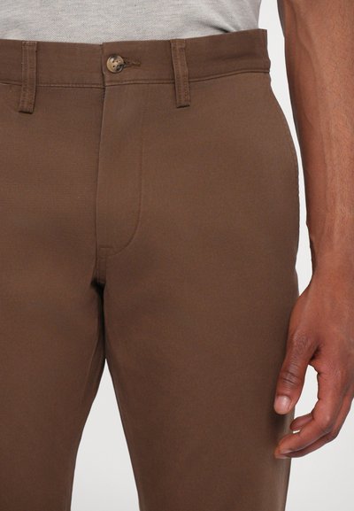Pantaloni in cotone marroni con una vestibilità standard, zip frontale, chiusura a bottone, tasche laterali e dettagli di cucitura minimi.