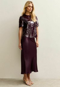 Bordowa sukienka z cekinowym, krótkim rękawem i gładką, satynową spódnicą. Strój ma lekki połysk i rozkloszowany fason.