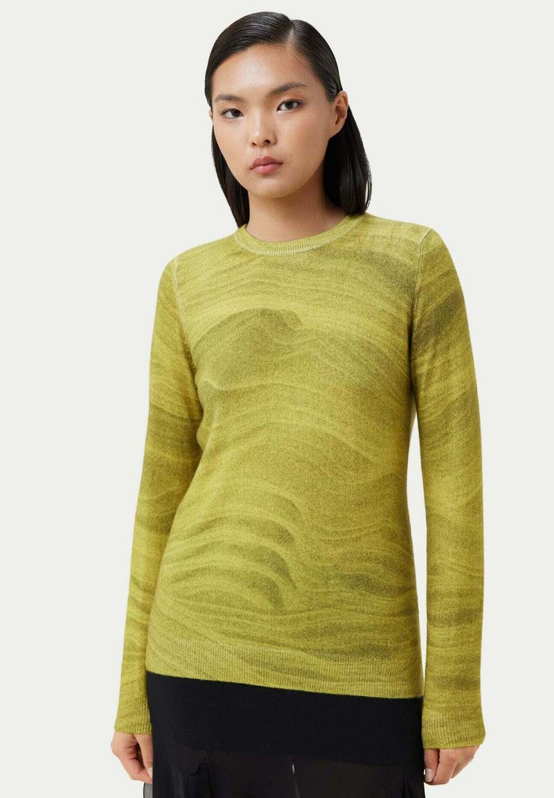 Gul ulltröja med ett subtilt vågigt mönster, långa ärmar och rund halsringning, tillsammans med en svart lagerkjol.