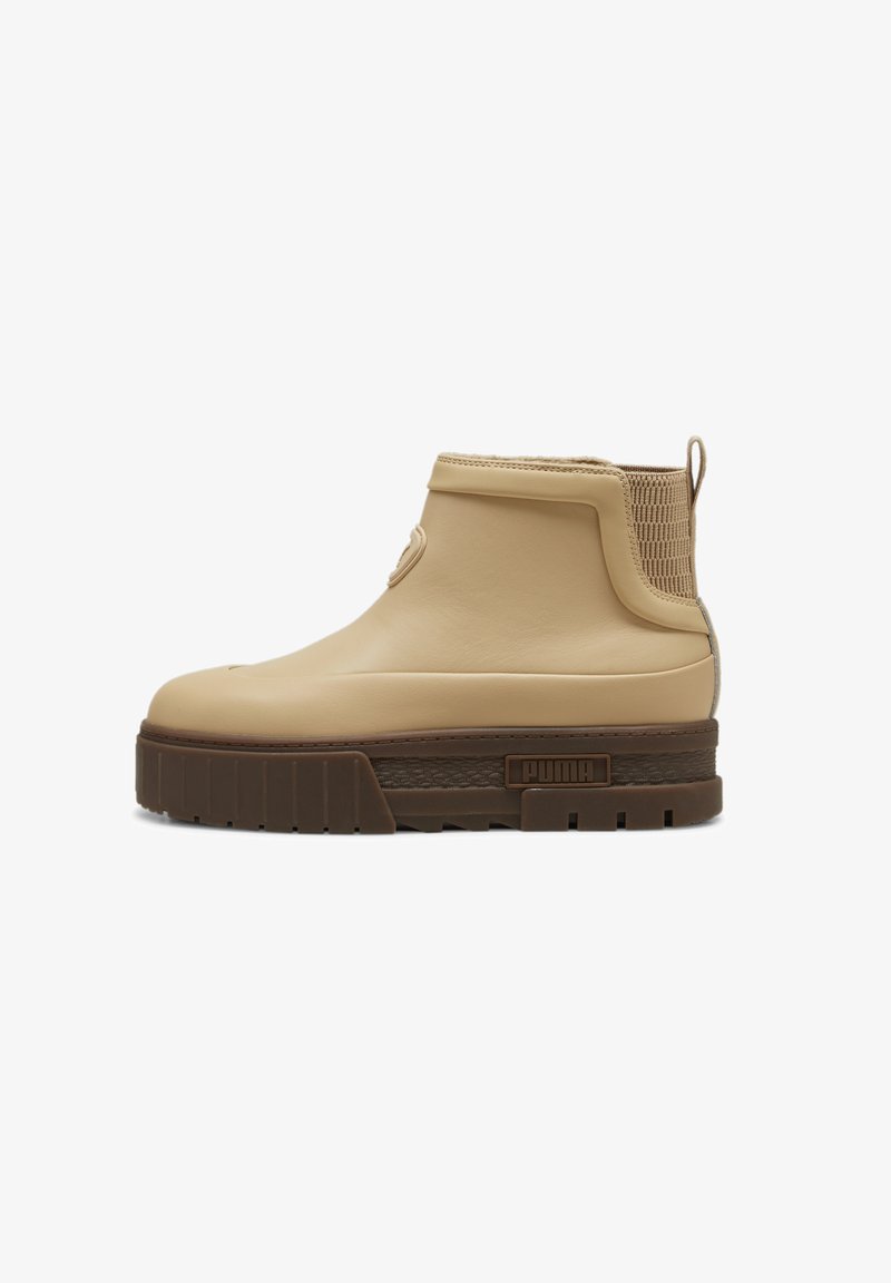 Beige ankelstøvle lavet af glat gummimateriale med en tekstureret mesh-sidesk panel og tyk brun sål; har et markant logo på siden.