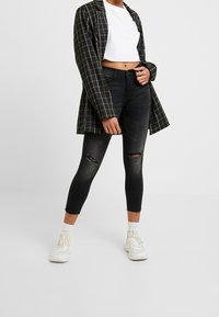 Svarta rivna skinny jeans med fransade kanter, kombinerat med en vit kortärmad t-shirt och en svart-vit rutig kavaj. Vita sneakers bärs.