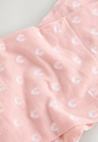 Blødt lyserødt stof med små hvide hjerte-mønstre, der viser blide folder og tekstur på en lys baggrund.