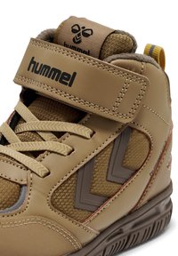 Beige højtop-sneakers med tekstureret stof og læderpaneler, udstyret med en Velcro-rem, kontrasterende brune detaljer og logodetaljer.