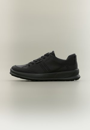 Zwarte lage sneaker met veters, geperforeerd zijdetail en gevoerde zool op een effen neutrale achtergrond.