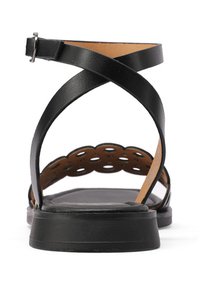 Sandalo in pelle nera con cinturini intrecciati, schienale aperto e un design con ritaglio circolare sulla cinghia del tallone. Suola piatta.