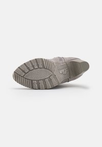 Semelle de chaussure en daim gris avec des bandeaux en caoutchouc texturés, présentant un motif distinct et un logo subtil. Design lisse et épuré.