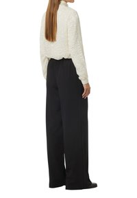 Cremfarbener Pullover mit Stehkragen, kombiniert mit lockeren schwarzen Hosen. Einfaches Design mit einer lässigen Silhouette.