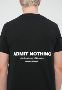 Zwart katoenen T-shirt met witte tekst op de achterkant die zegt "ADMIT NOTHING," met daaronder "Weekend Offender" en "LONDON, ENGLAND."