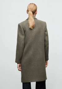 Abrigo de lana verde oliva con silueta recta, mangas largas y corte a medio largo. Diseño minimalista sin cierres ni patrones visibles.