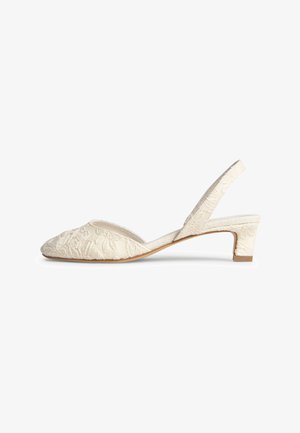 Zapato slingback color crema con tacón bajo de bloque, puntera puntiaguda y bordado floral texturizado en la parte superior de tela.