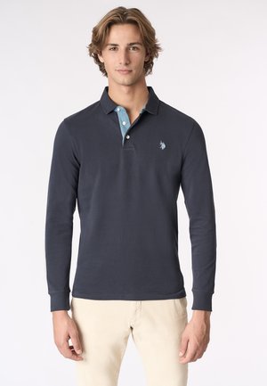 Polo a maniche lunghe di colore blu navy con colletto azzurro, dotato di tre bottoni e un piccolo logo sul petto. Tessuto in puro cotone morbido.