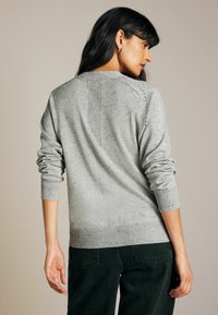 Lys gr�å sweater med struktureret strik, der har ribbede manchetter og kant. Bagsidedetaljer inkluderer lodrette sømme og et spraglet mønster.