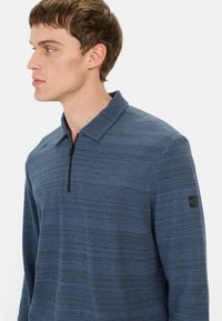 Granatowy sweter z kołnierzykiem i zapięciem na zamek, z teksturowanym wzorem i naszywką z logo na rękawie. Miękka tkanina.
