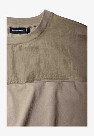 T-shirt beige à manches courtes avec un design à panneaux ton sur ton en tissu texturé. Comprend un col ras-du-cou côtelé et des détails de couture apparents.