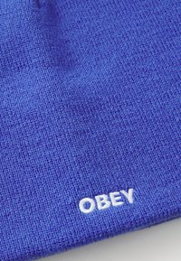 Beanie blu lavorato a maglia realizzato in tessuto testurizzato, con un logo ricamato bianco "OBEY" vicino al fondo. Design semplice e arrotondato.