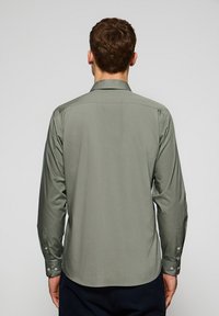 Camicia a maniche lunghe in verde oliva smorzato. Tessuto morbido con colletto classico, polsini abbottonati e orlo dritto sul retro.