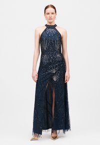 Abito da sera navy con collo halter, decorazioni in perline, uno spacco thigh-high, tulle a strati e una silhouette aderente. Calzature in tono oro.
