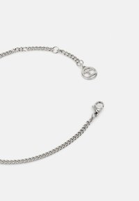 Pulsera de cadena de plata con un acabado suave, que presenta un charm circular y un cierre de langosta. Los eslabones son de tamaño mediano y bien definidos.