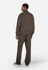 Brūns kokvilnas sporta krekls un atbilstoši bikses, brīvs piegriezums, ribota apkakle, maiga tekstūra, valkāts ar gaišām krāsām sporta apaviem.