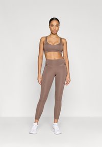 Smeđi atletski crop top i tajice visoki struk od glatkog materijala. Ima blizak fit i detalje šivanja; uparen s bijelim tenisicama.