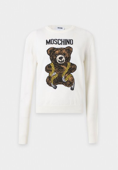 Pull blanc à manches longues avec un ours en peluche marron portant un ruban à mesurer jaune et le texte "MOSCHINO" au-dessus de l'ours.