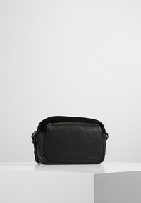 Mustakasi nahkainen olkalaukku suorakaiteen muotoinen, sileä pinta, vetoketjukiinnitys ja säädettävä hihna. Sisältää etutaskun.