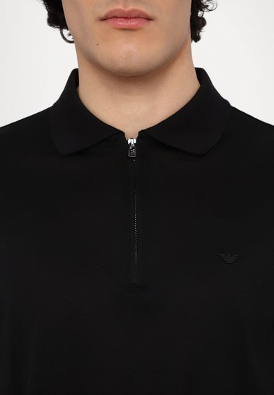 Μαύρο πουκαμίσo με φερμουάρ και μυτερό γιακά, διαθέτει ένα μικρό κεντημένο λογότυπο στο αριστερό στήθος και έχει λεία, ελαφριά υφή.