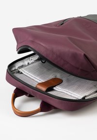 Zaino bordeaux con accenti grigi, dotato di una zip superiore e manico in pelle. All'interno, un vano in tessuto a griglia con una cintura in pelle beige.