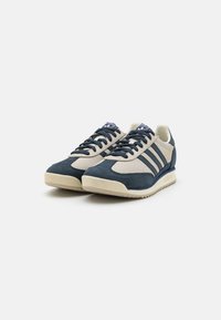 Blauwe en beige sportschoenen met een bovenwerk van suede en mesh, een getextureerde rubberen zool en drie laterale strepen. Rond neus met veters.