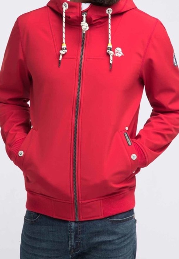 Homme portant une veste rouge zippée avec des cordons blancs, des poches latérales avec boutons-pression, et un petit logo sur la poitrine et la manche.