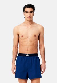 Boxers en coton bleu marine avec une texture solide, taille élastique arborant un logo blanc et une fermeture à bouton à l'avant.