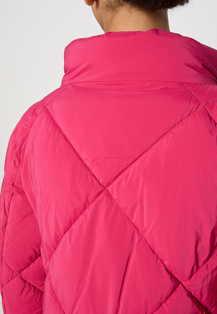 Fuchsia gesteppte Puffjacke mit hohem Kragen und diagonaler Nahtmusterung. Das Material scheint leicht und glatt zu sein.