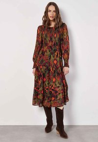 Langes, gemustertes Kleid mit gerafftem Oberteil, das florale Designs in Grün, Rot und Orange zeigt. Kombinieren Sie es mit braunen kniehohen Stiefeln.