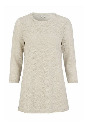 Blonde spids top i lys beige med trekvartærmer, rund halsudskæring og struktureret blomsterprint. Har en afslappet pasform og blødt materiale.