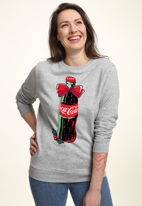Felpa grigia con un grande fiocco rosso e una grafica di una bottiglia di Coca-Cola decorata con foglie di agrifoglio, realizzata in morbido cotone.