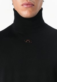 Μαύρο πουλόβερ με ζιβάγκο και ραβδωτή υφή, με μικρό λογότυπο στο κέντρο. Στενή σχεδίαση και λείο ύφασμα.