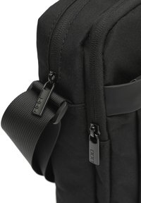 Borsa a tracolla nera in tessuto con superficie liscia, caratterizzata da un design elegante, chiusure con zip, tracolla regolabile e dettagli hardware minimalisti.
