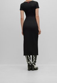 Robe midi côtelée noire à manches courtes, avec une étiquette logo rouge au-dessus de l'encolure arrière. Associée à des bottes noires et blanches montantes avec un motif d'éclair.
