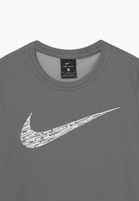 Camisa de entrenamiento Nike Dri-FIT gris con cuello redondo, tela texturizada y un logo de swoosh blanco con patrón en el frente. Etiqueta de talla M visible.