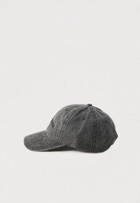 Worn black baseball cap with six panels and ventilation eyelets, embroidered text on front, placed on white surface.