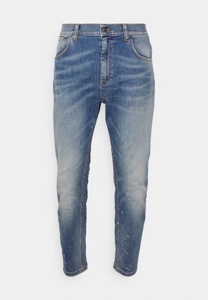 Siniset haalistuneet slim fit -farkut, joissa hieman kulutusta ja napin sekä vetoketjut sulkeminen, esitetty yksinkertaisella taustalla.