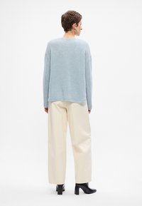 Jasnoniebieski sweter z dzianiny o teksturowanym wykończeniu, w zestawieniu z kremowymi spodniami typu wide-leg i czarnymi butami na słupku; prosty, czysty design.