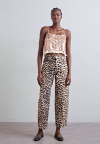 Top court en sequins rose doré avec des bretelles spaghetti, associé à un pantalon large beige à motifs léopard et des chaussures plates noires.