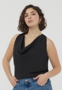 Top senza maniche nero con design a collo drappeggiato, realizzato in tessuto morbido. Indossato con jeans in denim blu a vita alta.